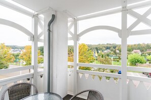 A covered balcony with white railings, wicker chairs, and a glass table. - Perfekt fur Familien - Grosse Ferienwohnung mit Balkon in Sellin (Sellin)