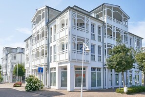 A white building with a shop on the ground floor and a balcony. - Perfekt fur Familien - Grosse Ferienwohnung mit Balkon in Sellin (Sellin)