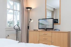 Ein Hotelzimmer mit einem Bett, einem Nachttisch mit Flachbildfernseher, einer Lampe und einem Fenster mit Vorhängen.