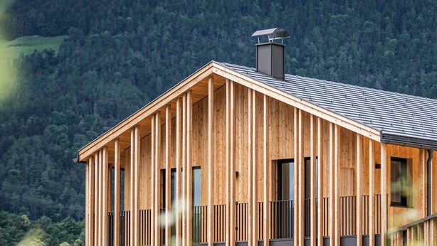 Moderni puinen mökki, jossa on parveke, ja se sijaitsee metsäisen rinteen keskellä.