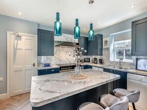 Une cuisine moderne avec un îlot en marbre, des armoires bleues et des luminaires suspendus.