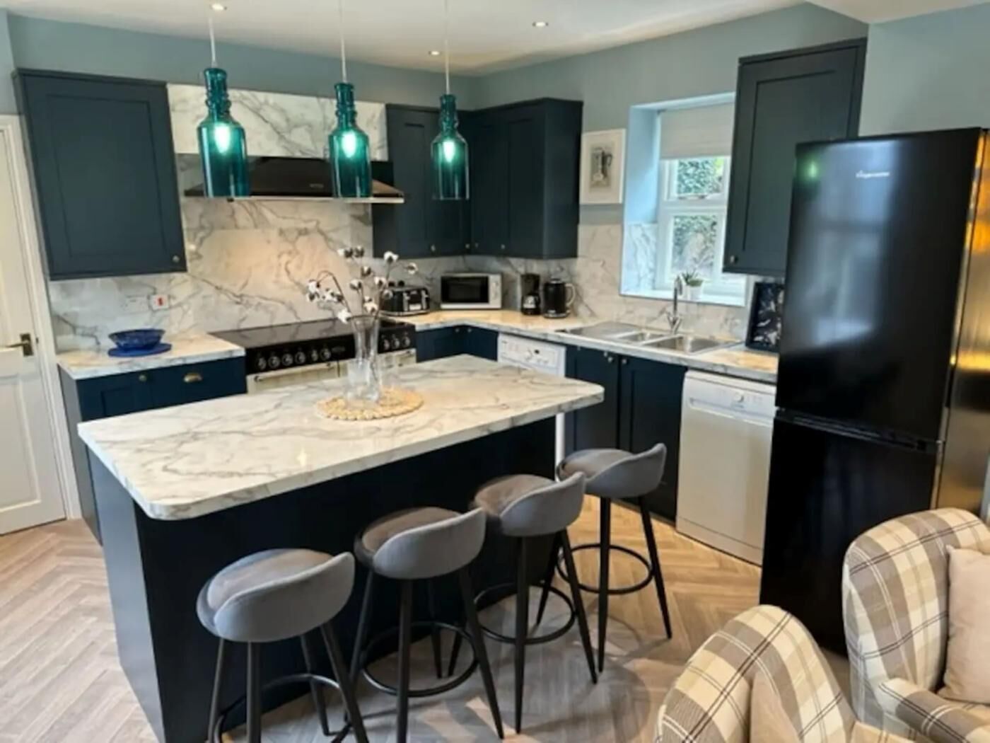 A modern kitchen with dark cabinets, a marble island, bar stools, and a black refrigerator.
