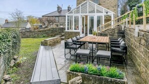 Un patio con tavolo e sedie in legno, una struttura in vetro e un muro in pietra.
