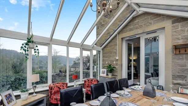 Una veranda con un tavolo da pranzo imbandito per sei persone, circondata da pareti in pietra e ampie finestre.