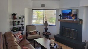 A living room with a sofa, armchair, coffee table, fireplace, TV, bookshelf, and a ceiling fan. - Peaceful and quiet 1-bedroom condo with AC in charming Borrego Springs (Borrego Springs)