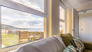 A room with a large window, a sofa with striped pillows, and a view of a beach. - 2 Bed in Braunton (oc-87111) (Croyde)