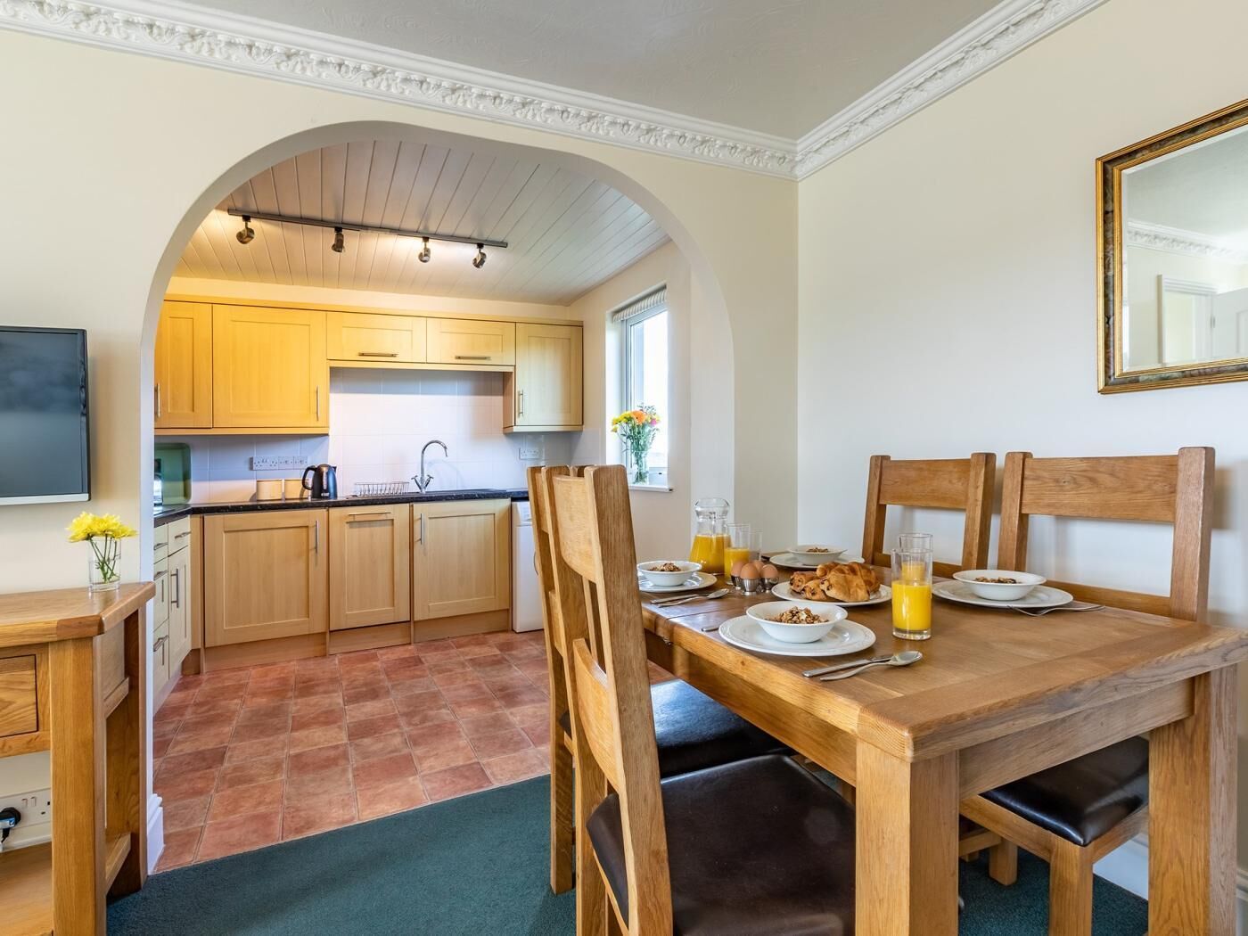 A kitchen with wooden cabinets, a dining table with chairs, and breakfast items.