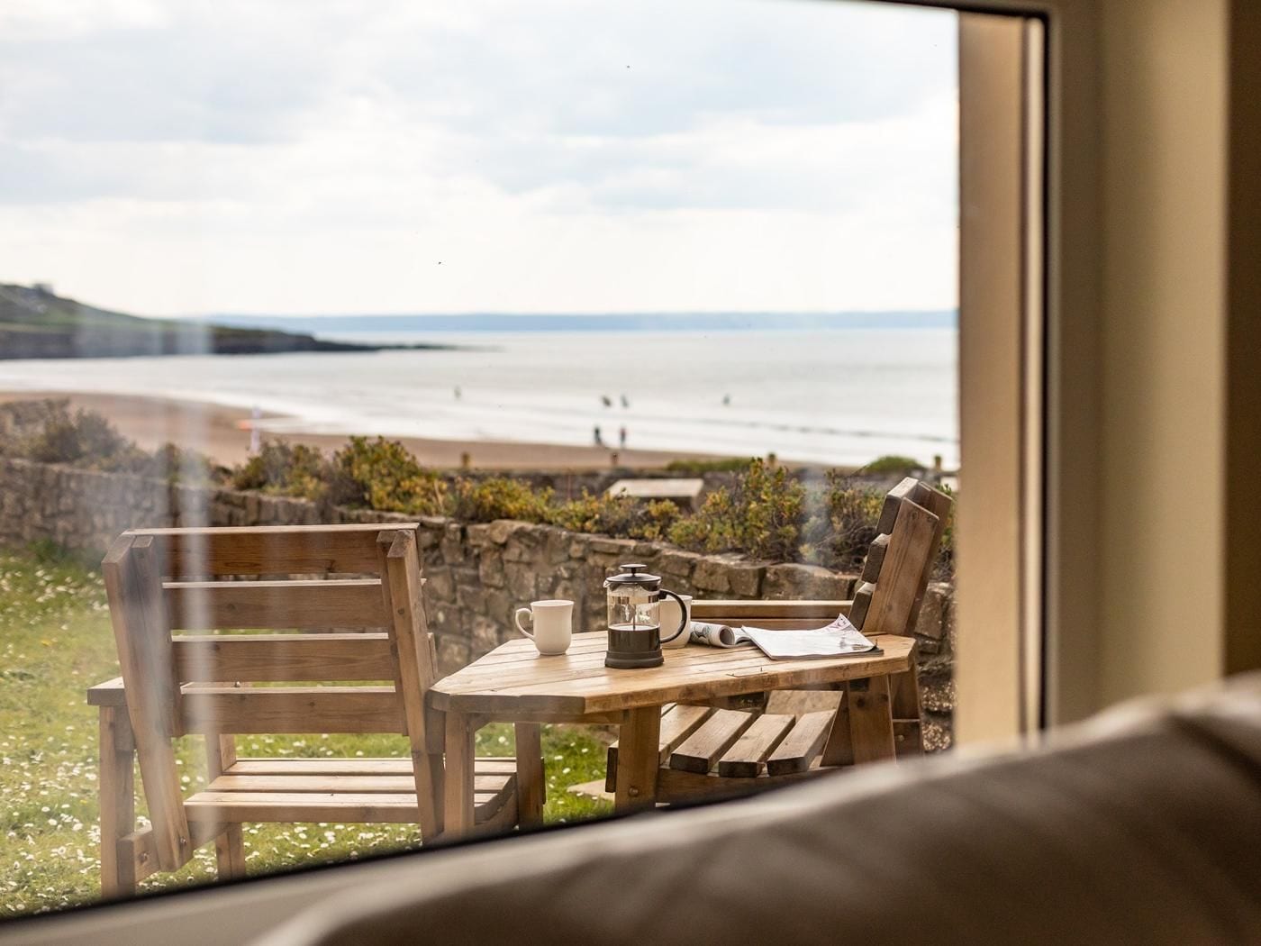 A wooden table with chairs and a view of a beach through a window.