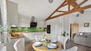 Et moderne køkken med hvide skabe, en grøn backsplash og et spiseområde med et træbord dækket til fire personer.