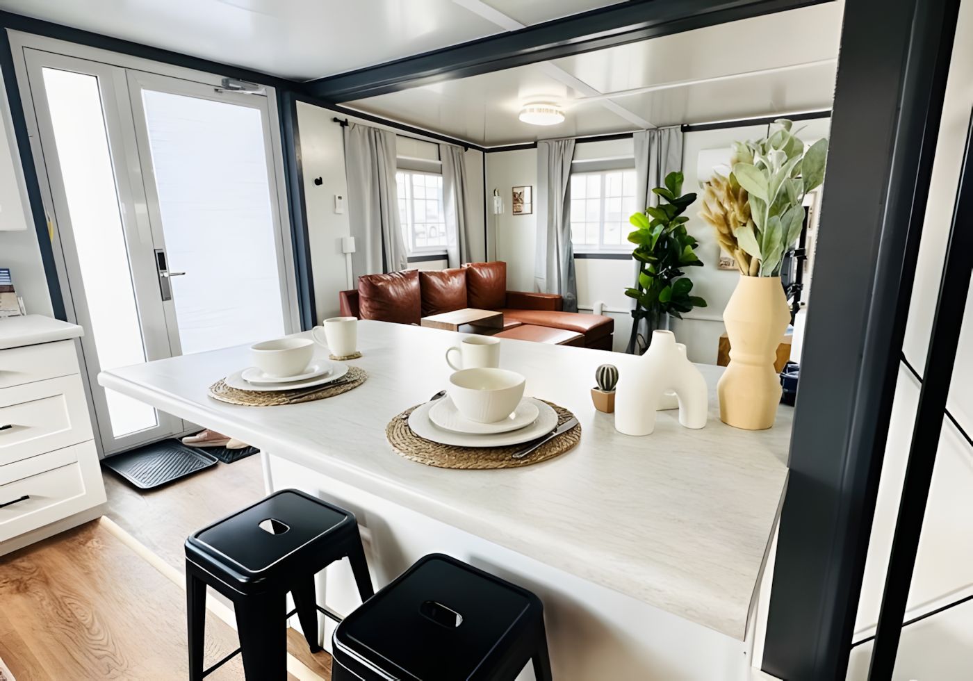 A modern kitchen with a central island, two black stools, and a dining area with a brown leather couch.