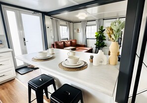 Una cocina moderna con una isla central, dos taburetes negros y una zona de comedor con un sofá de cuero marrón.