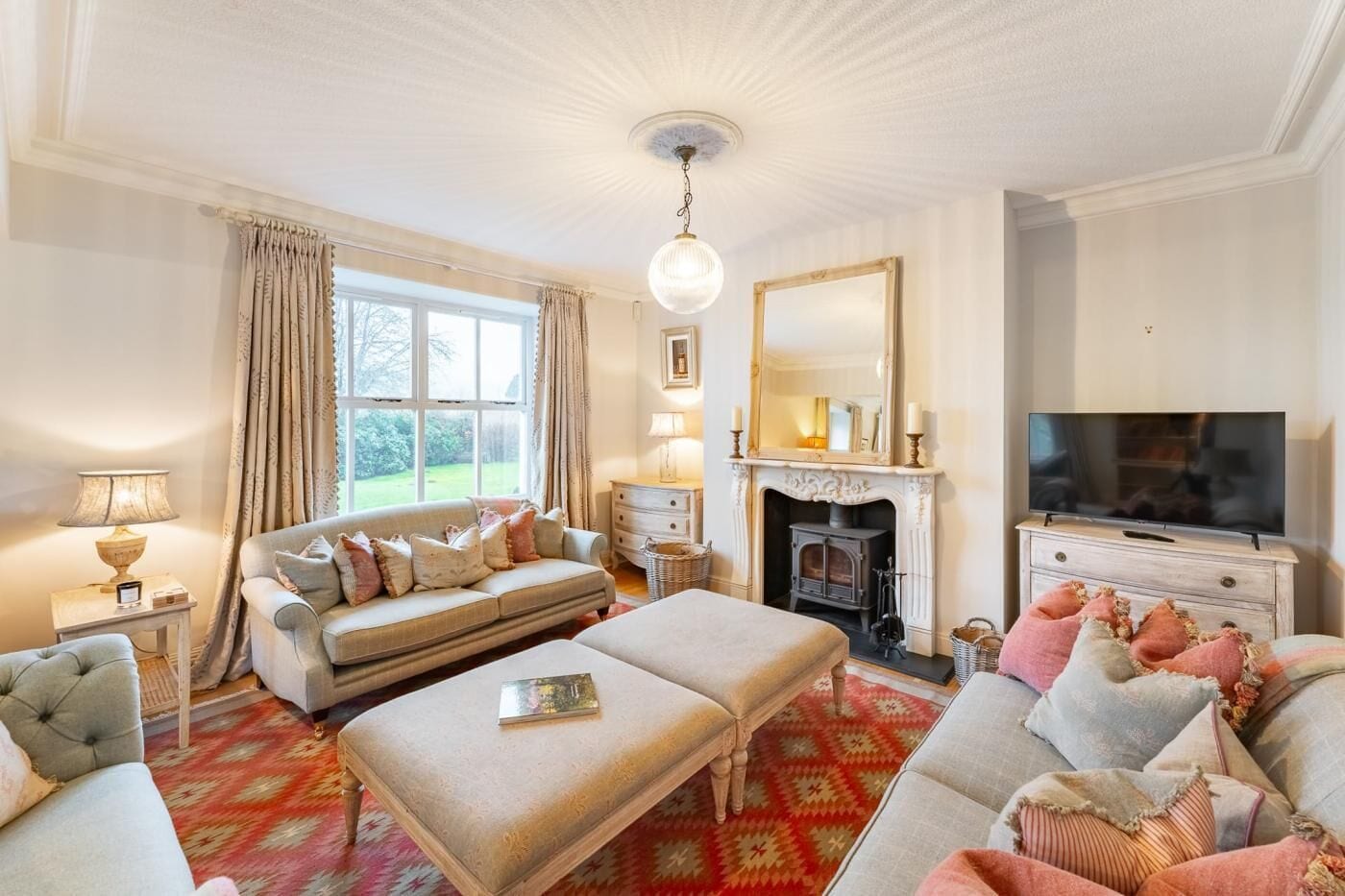A traditional living room with a sofa, ottoman, fireplace, television, and a large window.