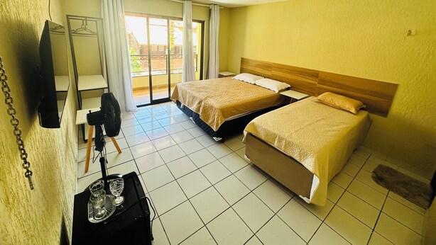 Habitación de hotel con dos camas, televisión, ventilador y vista al exterior.