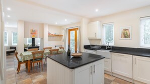 A modern kitchen with white cabinets, a black countertop, and a dining area with a table and chairs. - 1 Bed in Skelwith Bridge (oc-lr159) (Skelwith)