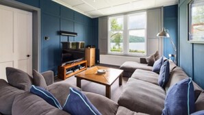 A living room with a sofa set, a TV, and a window with a view of a lake. - 5 Bed in Taynuilt (oc-ca008) (Kilchrenan)