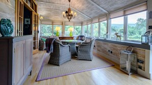 A dining area with wicker furniture, a chandelier, and large windows with a view. - 5 Bed in Taynuilt (oc-ca008) (Kilchrenan)