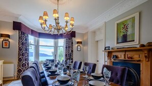 A dining room with a long table set for a meal, a chandelier, and a fireplace. - 5 Bed in Taynuilt (oc-ca008) (Kilchrenan)