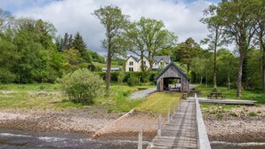 A wooden bridge leading to a rustic building with a covered area, surrounded by greenery and a river. - 5 Bed in Taynuilt (oc-ca008) (Kilchrenan)