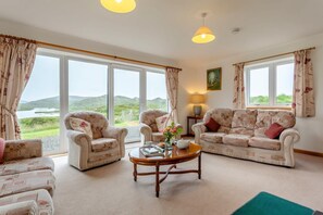 A spacious living room with large windows, floral-patterned furniture, and a view of the outdoors. - 4 Bed in Lairg (oc-ca417) (Lochinver)