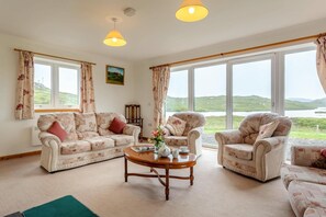 A living room with a sofa set, two armchairs, a coffee table, and large windows offering a view of the outdoors. - 4 Bed in Lairg (oc-ca417) (Lochinver)