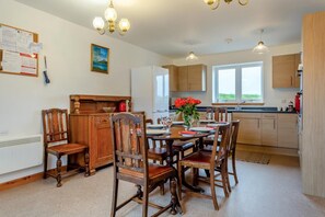 A dining area with a wooden table and chairs, a painting on the wall, and a window with a view. - 4 Bed in Lairg (oc-ca417) (Lochinver)