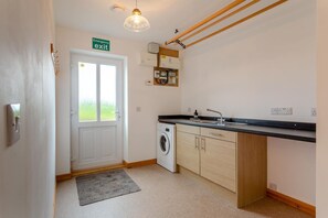 A compact kitchen with a washing machine, a sink, and a wooden countertop. - 4 Bed in Lairg (oc-ca417) (Lochinver)