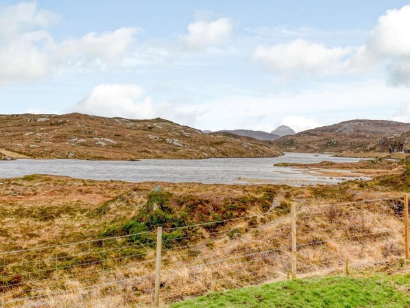 A natural landscape with a body of water, hills, and a fenced area.