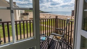 En balkong med utsikt över en strand, en stol och en hatt som ligger på räcket.