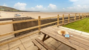 Uitzicht op het strand met een houten terras, een picknicktafel en een boek getiteld 'The Secret Life of the Beach'.
