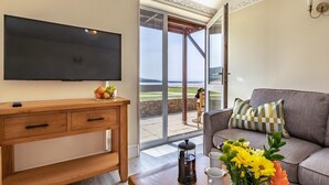 Ein Wohnzimmer mit Fernseher, Holzschreibtisch, Sofa und Blick ins Freie.