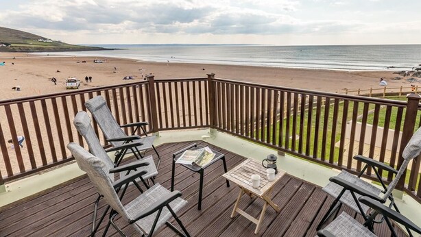 Terraza de madera con sillas y una mesa con vista a la playa.