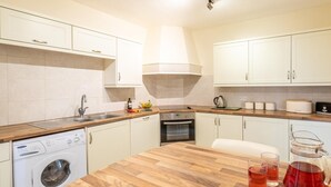 Cocina moderna con encimera de madera, electrodomésticos integrados y una isla central con tetera y vasos.
