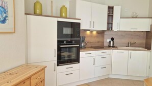 Cocina compacta con armarios blancos, horno empotrado, cafetera y lavamanos.