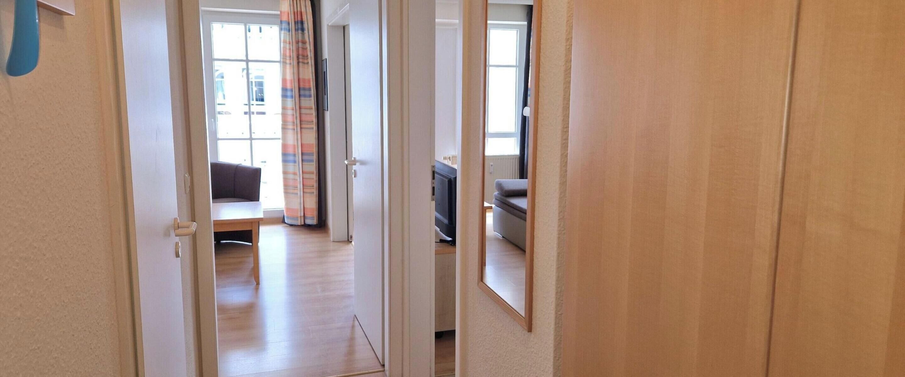 A hallway leading to a living room with a sofa, a television, and a window with curtains.