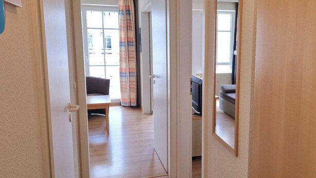 Un pasillo que conduce a una sala de estar con un sofá, un televisor y una ventana con cortinas.