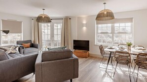 A modern living room with a sofa, TV, dining table, and wicker chairs. - 3 Bed in Braunton (oc-87754) (Croyde)