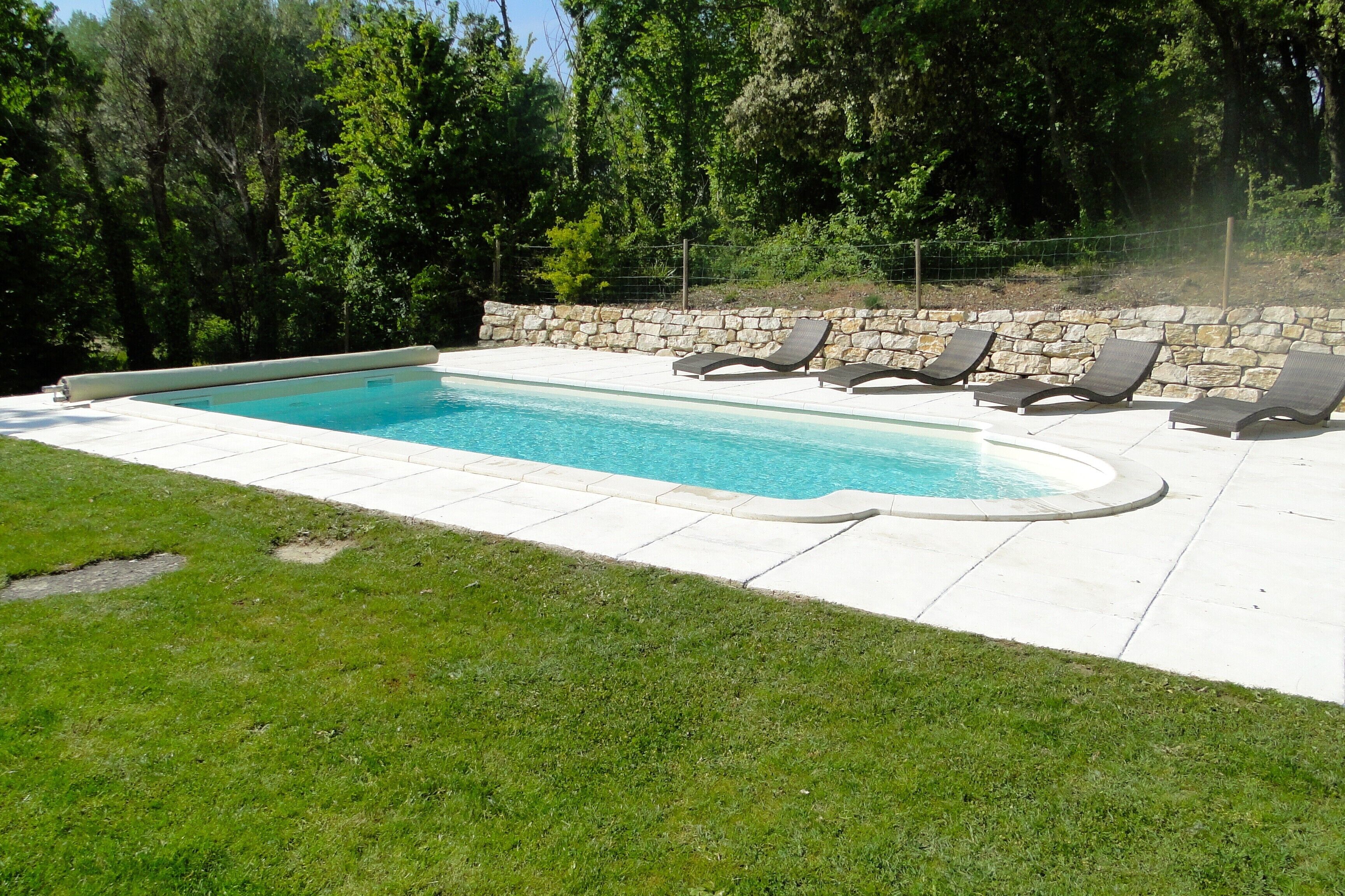 Ein rechteckiger Pool mit einer Steinmauer und Liegestühlen.