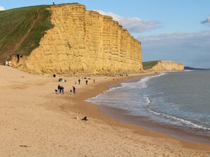 A beach with a large cliff, sandy shore, and people walking along the beach. - 2 Bed in Bridport (oc-dc191) (Askerswell)