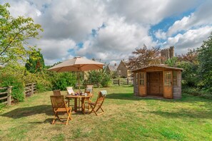 A rustic outdoor dining area with a table and chairs, a wooden structure, and a stone building in the background. - 2 Bed in Bridport (oc-dc191) (Askerswell)