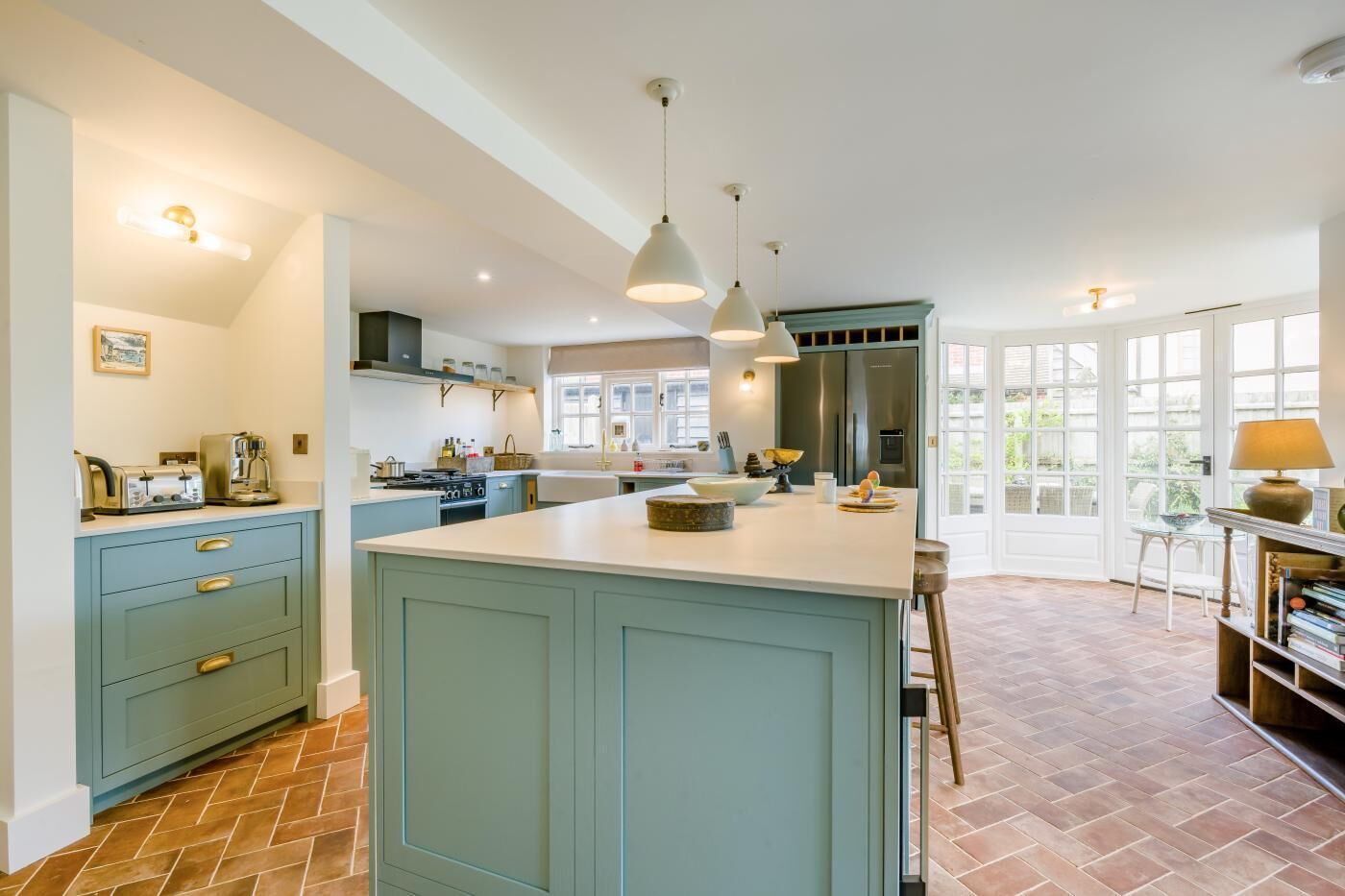 A kitchen with a central island, a dining area with a table and chairs, and a view through large windows.