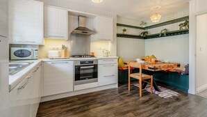 Una cocina moderna con armarios blancos, horno empotrado y un comedor con mesa y sillas de madera.