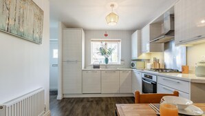 Una cocina moderna con armarios blancos, una mesa de comedor con un vaso de jugo de naranja y una lámpara colgante.