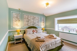 A bedroom with a bed, two bedside lamps, a window with a view, and framed artwork on the wall. - 2 Bed in Thornton (oc-h36043) (Thornton)