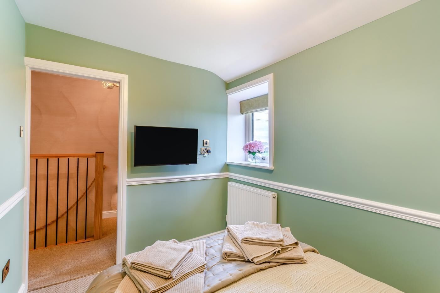 Quarto com cama, televisão na parede, janela com vista e porta para outro cômodo.