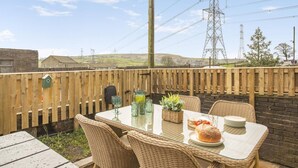An outdoor patio with wicker furniture, a table set with plates, glasses, and a pitcher, and a view of the countryside. - 2 Bed in Thornton (oc-h36043) (Thornton)
