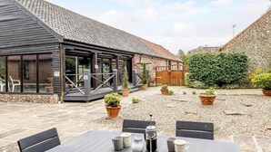 A rustic building with a stone facade, a wooden deck, and a patio area with outdoor seating. - 3 Bed in Toftrees (oc-kt076) (Toftrees)