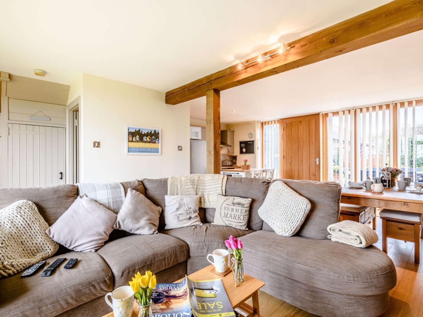 A cozy living room with a large sofa, a coffee table with books and flowers, and a kitchen in the background.