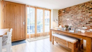 A modern kitchen with wooden cabinets, a dining table, and a brick accent wall. - 3 Bed in Toftrees (oc-kt076) (Toftrees)