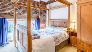 A four-poster bed with a view of a brick wall and a window with blue curtains. - 3 Bed in Toftrees (oc-kt076) (Toftrees)