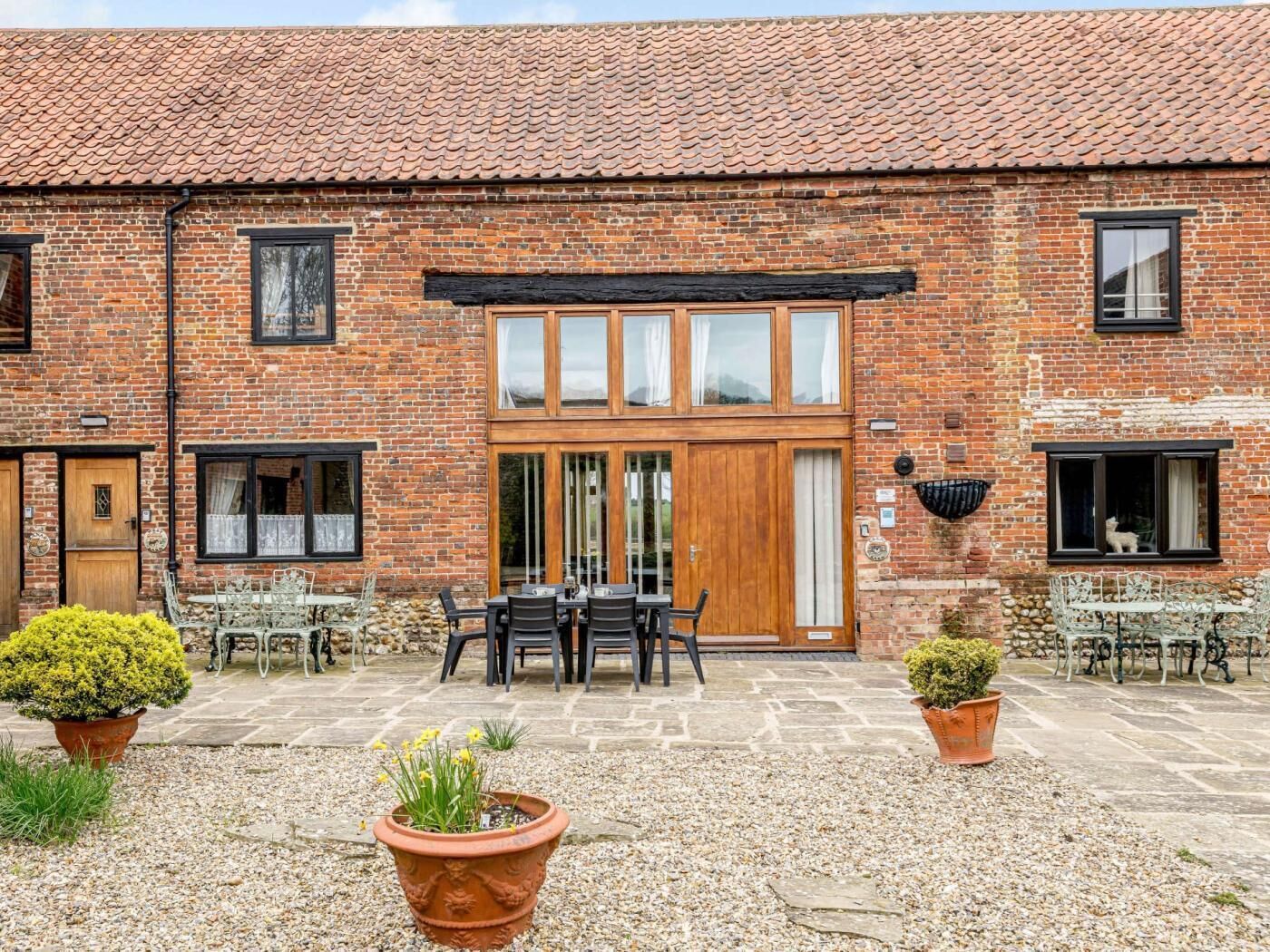 A brick building with a tiled roof, a wooden door, and a patio area with tables and chairs.